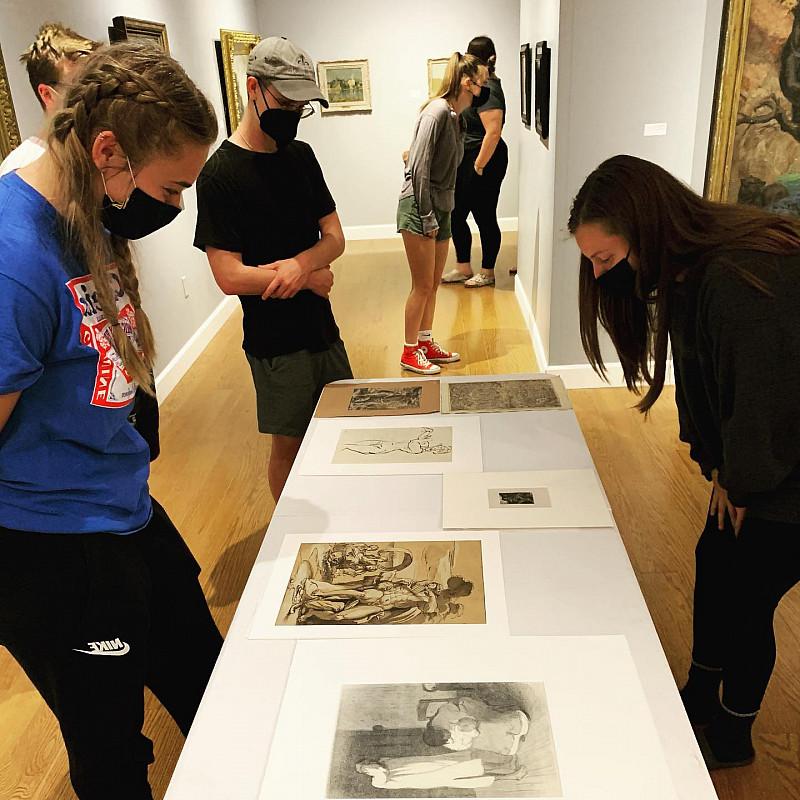 Students standing in the Wright Museum of Art gallery looking at art work on a table and on the walls.